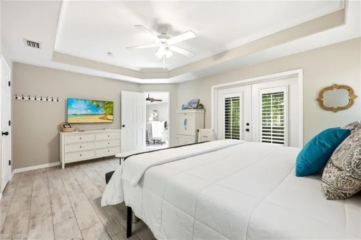 Spacious bedroom featuring wood-finish flooring, a tray ceiling with crown molding, and a ceiling fan