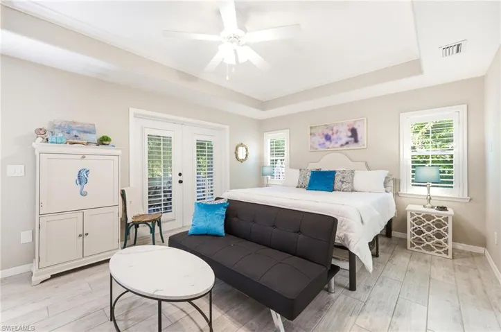 Tray ceiling featuring a ceiling fan, dual windows with plantation shutters, wood-finish flooring, and French doors