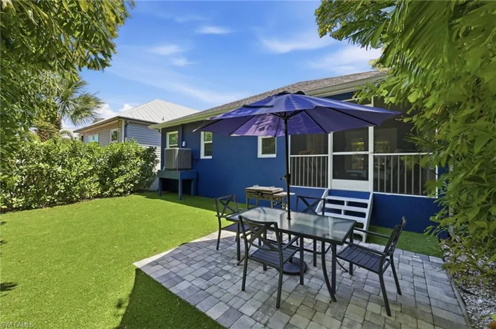 Paver patio and artificial turf lawn featuring a privacy hedge, dark blue exterior, and a screened porch