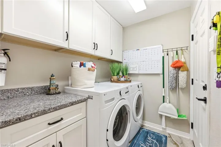Dedicated laundry area featuring white shaker-style cabinetry with matte black hardware, a granite-finish countertop, and durable wood-look flooring