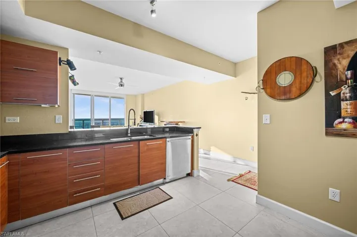 Kitchen featuring ceiling fan, dishwasher, light tile patterned flooring, and dark stone counters