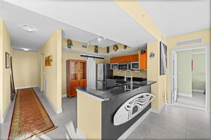 Kitchen with a barn door, track lighting, a peninsula, appliances with stainless steel finishes, and light tile patterned flooring