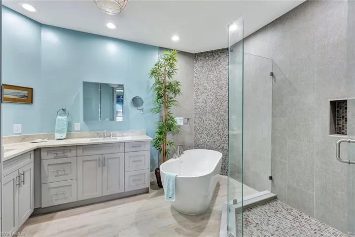 Bathroom with spacious updated vanity with added storage dual sinks, walk-in shower with glass shower enclosure, and tile walls.