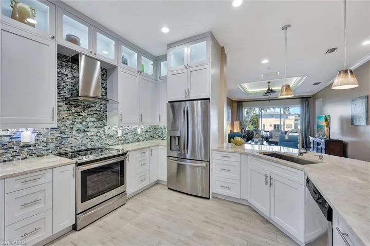 Modern Chef's kitchen with stainless steel appliances, white cabinetry, wall chimney exhaust hood, and sink