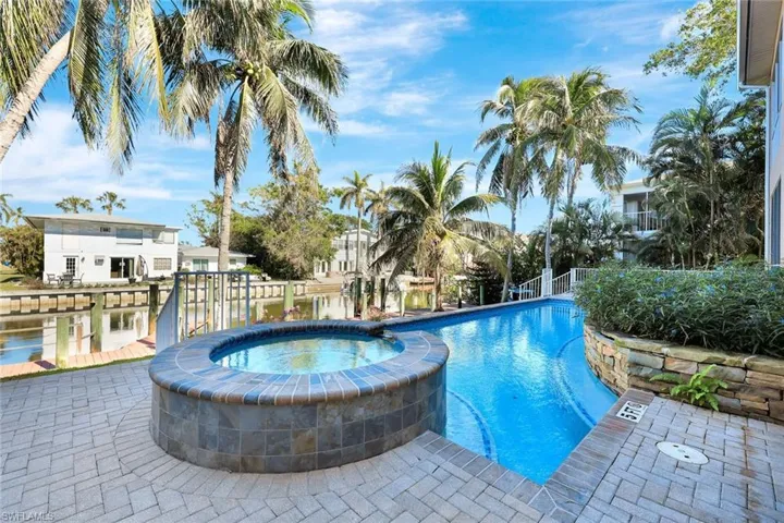 View of pool featuring a brick paver open patio, a water  and dock view, and a hot tub. Steps down to a sun deck area and to the boat docks.