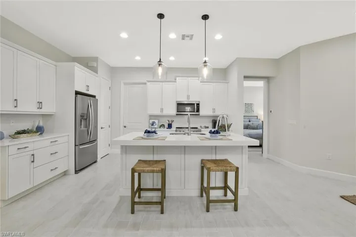 Kitchen with appliances with stainless steel finishes, white cabinetry, a breakfast bar area, decorative light fixtures, and a kitchen island with sink