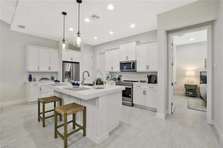 Kitchen with a kitchen breakfast bar, appliances with stainless steel finishes, white cabinets, pendant lighting, and a kitchen island with sink