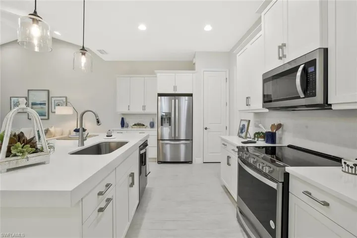 Kitchen featuring stainless steel appliances, white cabinets, decorative light fixtures, a center island with sink, and recessed lighting
