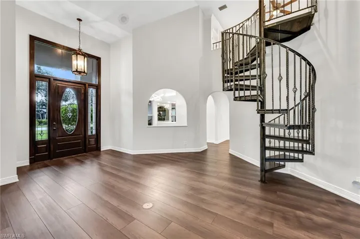 Two-story foyer with wood-finish flooring, a wrought iron spiral staircase, arched wall openings, and a prominent dark wood entry door with leaded glass