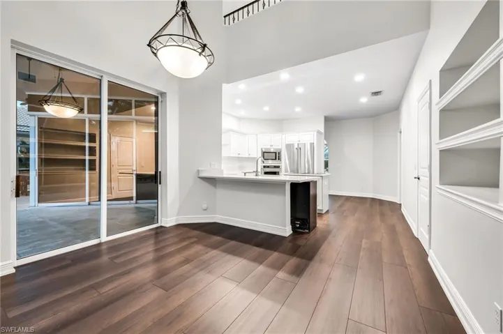 Volume ceilings, wood-finish flooring, built-in shelving, white cabinetry, and stainless steel appliances