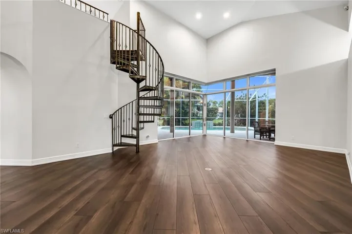 Grand spiral staircase with wrought iron balusters, soaring volume ceilings, expansive window wall, wood-finish flooring, and recessed lighting