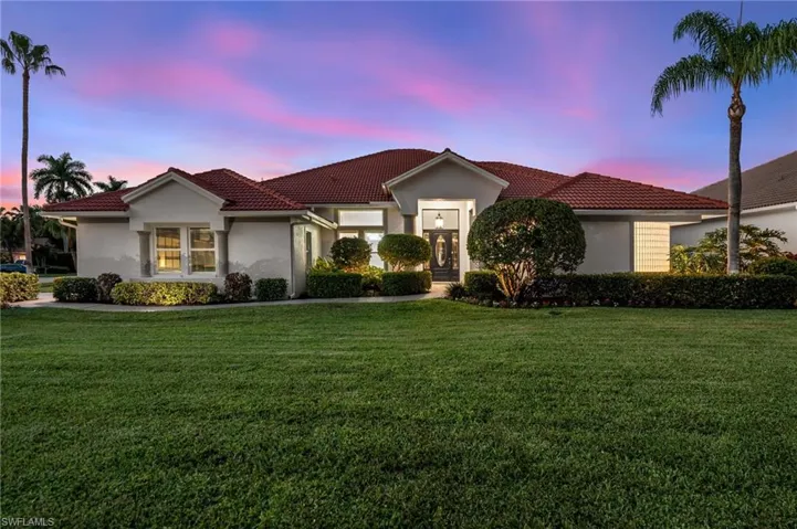 Stucco exterior featuring a tiled roof, mature landscaping, a prominent entry, and a well-maintained lawn