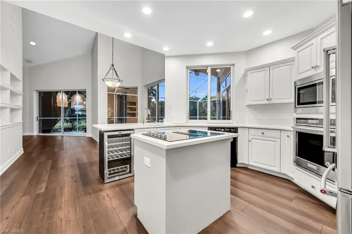 Volume ceilings, wood-finish flooring, built-in shelving, white cabinetry, and stainless steel appliances