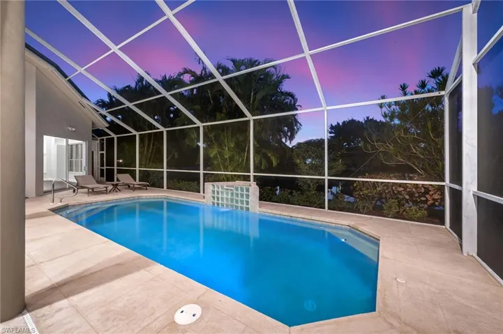 Screened enclosure with an in-ground swimming pool, surrounding stone-finish decking, and an integrated water feature