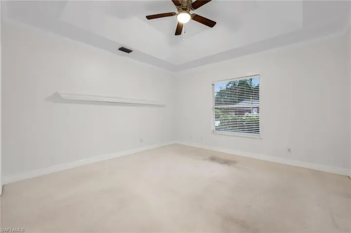 Tray ceiling with a ceiling fan, window with blinds, and wall-mounted shelving
