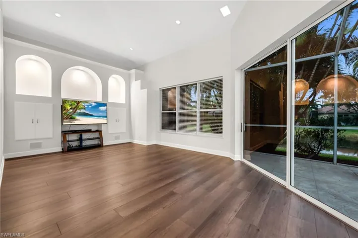 Volume ceiling, recessed lighting, wood-finish flooring, built-in wall niches with integrated lighting, and sliding glass doors