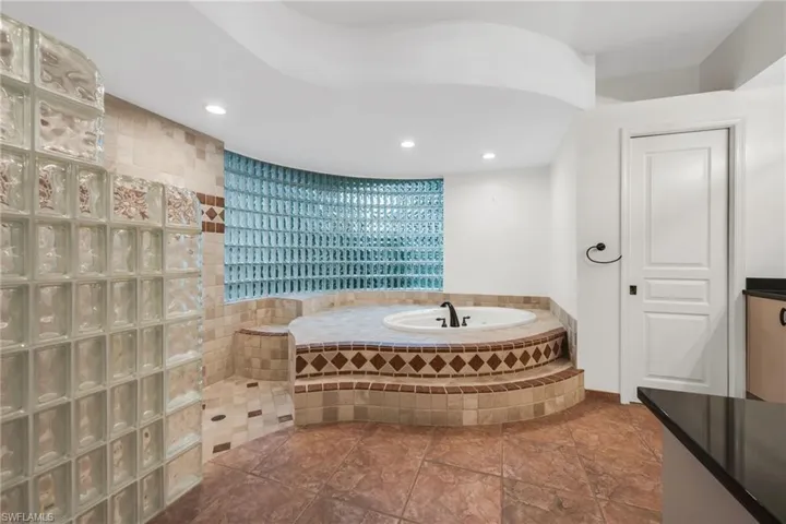 Built-in soaking tub with tiled surround, glass block wall feature, recessed lighting, and tiled flooring