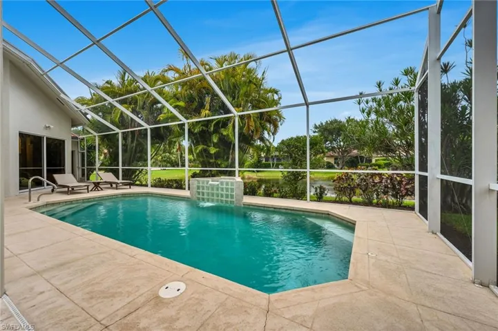 Screened-in pool enclosure featuring a rectangular pool with integrated steps and a water feature