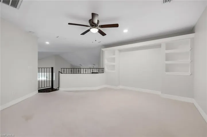 Built in shelves with white carpet and ceiling fan.