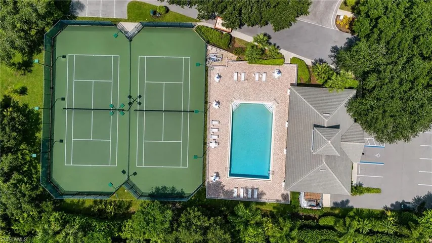 Two hard-surface tennis courts with perimeter fencing, a rectangular swimming pool with paved surround, and a building with a multi-gabled roof