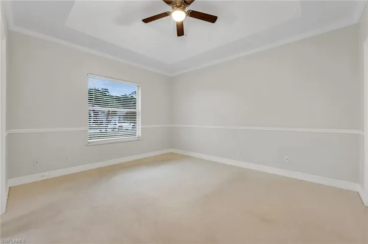 Recessed ceiling detail, ceiling fan with integrated lighting, window with blinds, decorative chair rail molding, and neutral wall tones