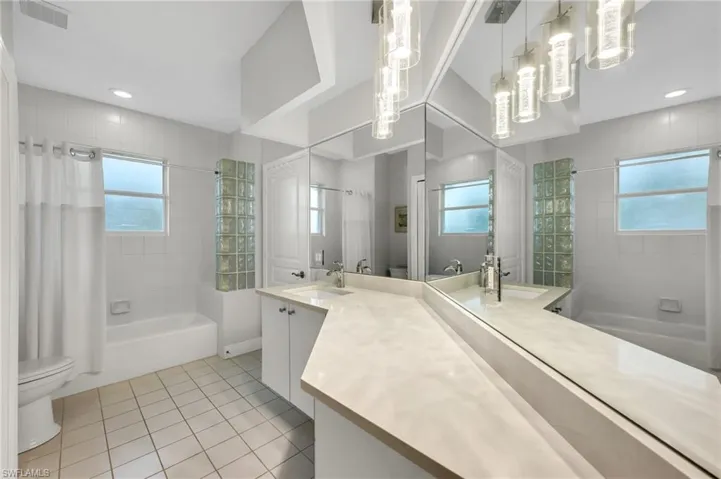 Dual vanity with stone-finish countertop, full-height wall mirror, recessed lighting, and a bathtub with glass block partition