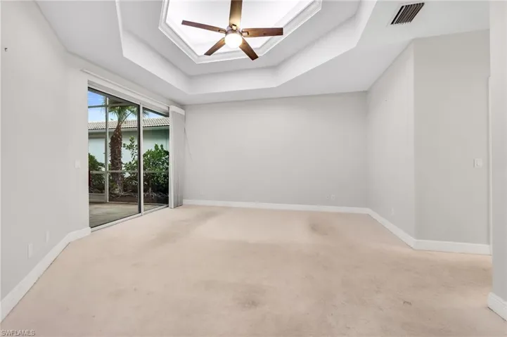Tray ceiling with a ceiling fan, light-colored carpeting, sliding glass doors, and recessed lighting