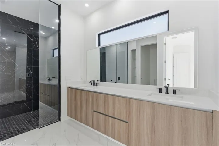 Bathroom featuring double vanity, a marble finish shower, light marble finish flooring, and recessed lighting