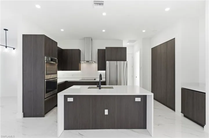 Kitchen featuring modern cabinets, light stone counters, a center island with sink, dark brown cabinets, and recessed lighting