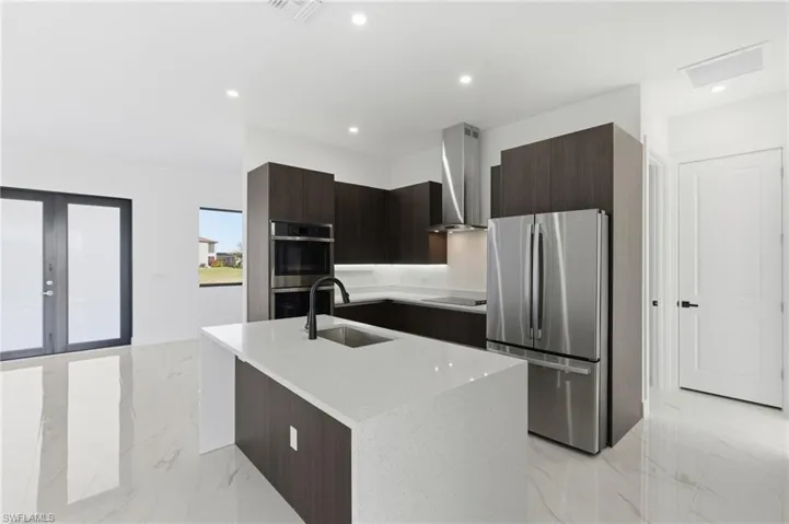 Kitchen featuring modern cabinets, appliances with stainless steel finishes, dark brown cabinets, an island with sink, and recessed lighting