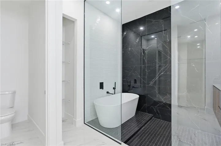 Bathroom with a freestanding bath, marble finish flooring, a marble finish shower, a spacious closet, and recessed lighting