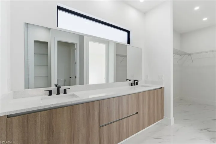 Bathroom featuring a spacious closet, double vanity, light marble finish floors, and recessed lighting