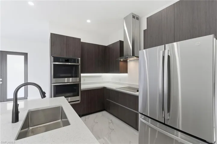 Kitchen with stainless steel appliances, modern cabinets, light marble finish flooring, wall chimney exhaust hood, and recessed lighting