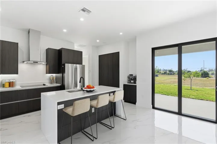 Kitchen featuring modern cabinets, a breakfast bar, a center island with sink, wall chimney range hood, and freestanding refrigerator