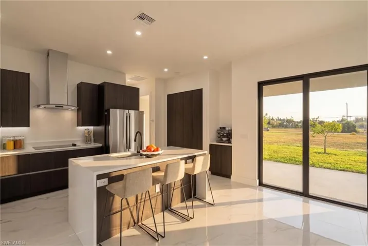 Kitchen featuring a breakfast bar area, modern cabinets, wall chimney range hood, a kitchen island with sink, and freestanding refrigerator
