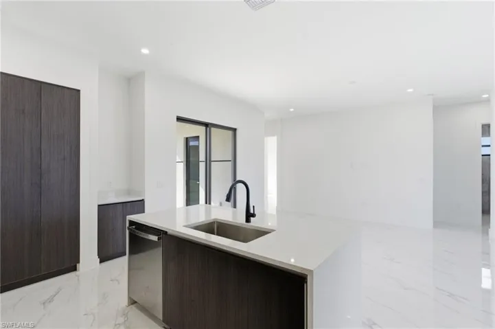 Kitchen with modern cabinets, light marble finish floors, dark brown cabinets, an island with sink, and stainless steel dishwasher