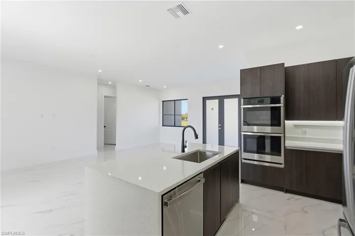 Kitchen featuring light marble finish flooring, modern cabinets, stainless steel appliances, recessed lighting, and an island with sink