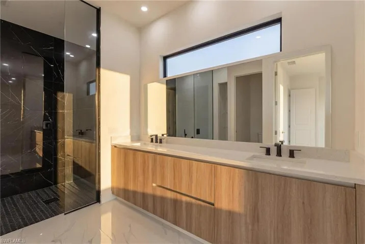 Bathroom with light marble finish floors, a marble finish shower, double vanity, and recessed lighting
