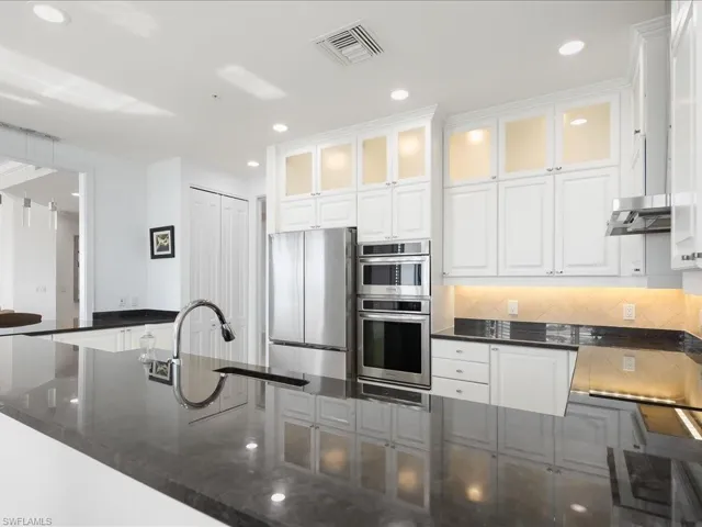 Kitchen with dark stone counters, glass insert cabinets, white cabinetry, freestanding refrigerator, and recessed lighting