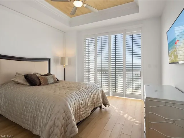 Bedroom featuring hardwood / wood-style floors, a raised ceiling, a ceiling fan, and ornamental molding