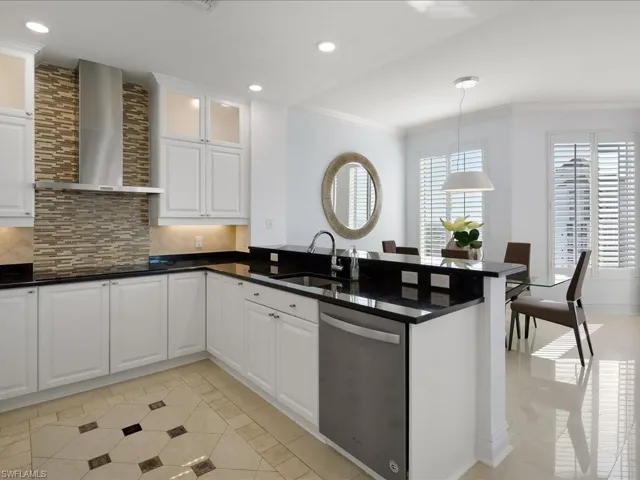 Kitchen featuring white cabinets, backsplash, stainless steel dishwasher, wall chimney range hood, and crown molding
