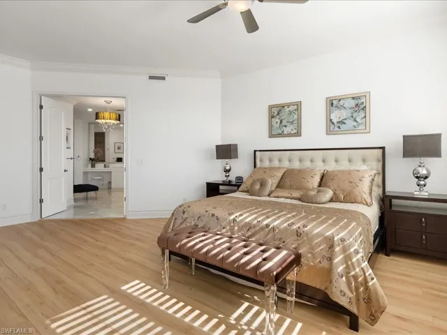 Bedroom featuring light wood finished floors, crown molding, a chandelier, ceiling fan, and ensuite bathroom