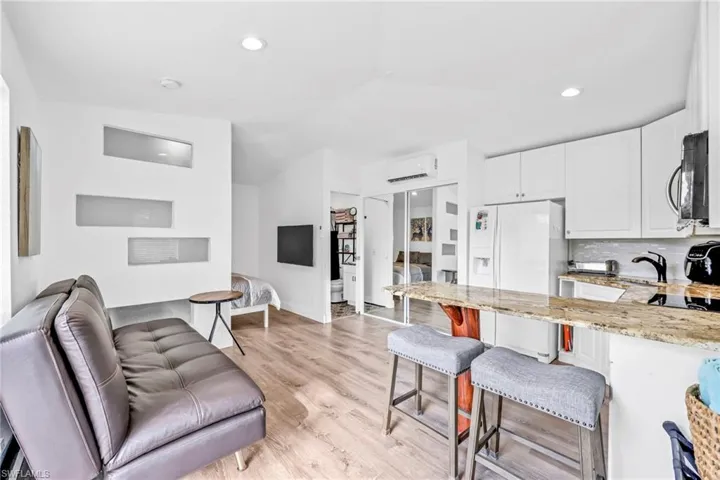 Kitchen with a breakfast bar area, light stone countertops, a peninsula, white fridge with ice dispenser, and light wood-type flooring