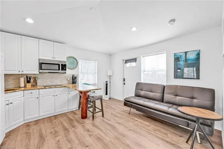 Kitchen featuring a breakfast bar, light stone countertops, light wood-style flooring, white cabinets, and stainless steel microwave