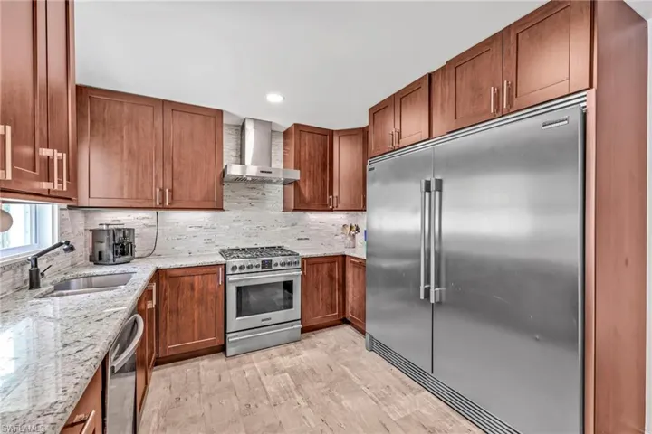 Kitchen with stainless steel appliances, light stone countertops, backsplash, light wood-type flooring, and recessed lighting