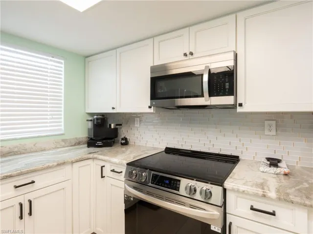White shaker cabinetry, stone countertops, stainless steel microwave, glass tile backsplash, and a flat-top electric range