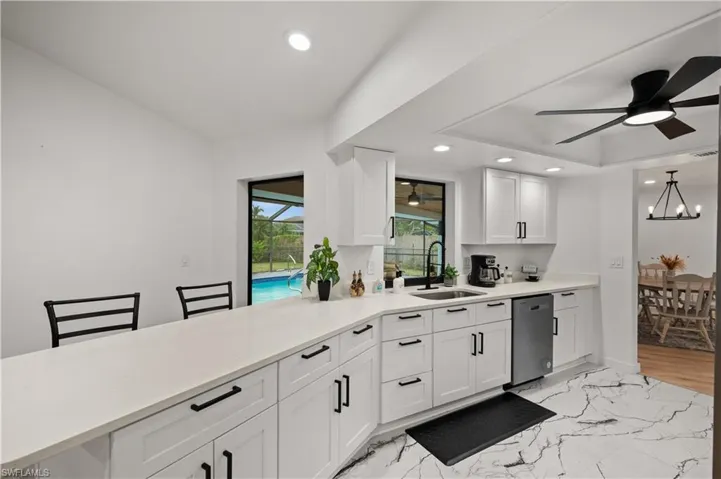 Kitchen featuring kitchen peninsula, stainless steel dishwasher, ceiling fan with notable chandelier, sink, and white cabinetry