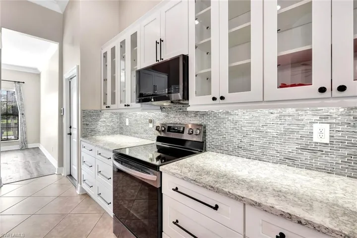 Kitchen featuring white cabinetry, stainless steel appliances, light stone counters, decorative backsplash, and light tile patterned flooring