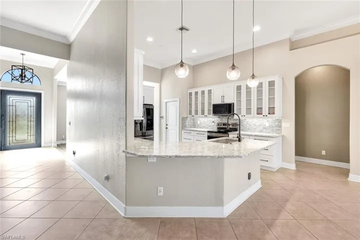 Kitchen featuring white cabinets, light stone counters, pendant lighting, light tile patterned flooring, and appliances with stainless steel finishes