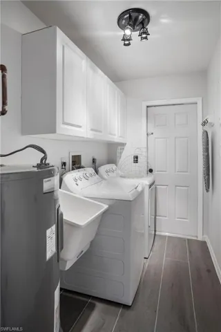 Clothes washing area with cabinets, washer and clothes dryer, water heater, and dark hardwood / wood-style flooring